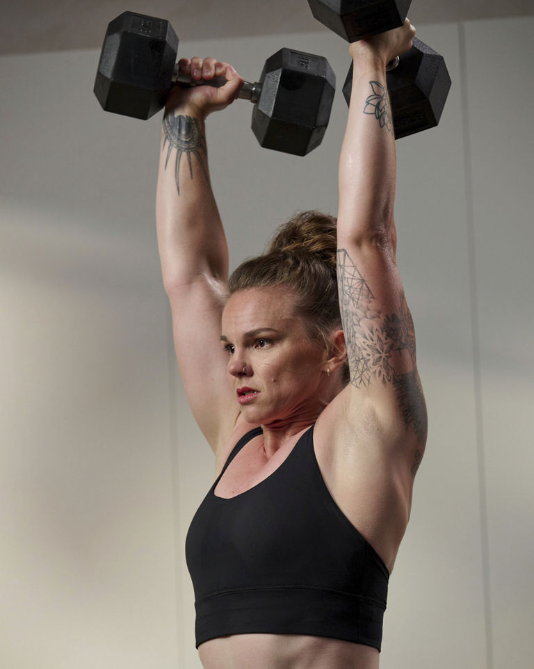 a woman doing a double dumbell overhead