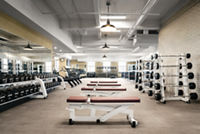 A brightly lit Life Time fitness floor with rows of hand weights, racked barbells and weight benches