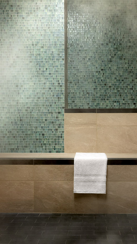 A luxury steam room with green and beige tile walls and a stack of white towels