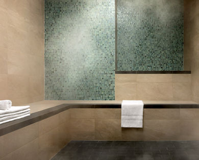 A luxury steam room with green and beige tile walls and a stack of white towels