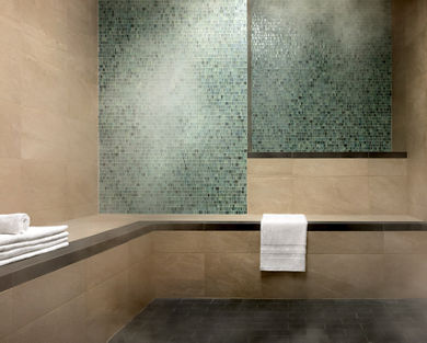 A luxury steam room with green and beige tile walls and a stack of white towels