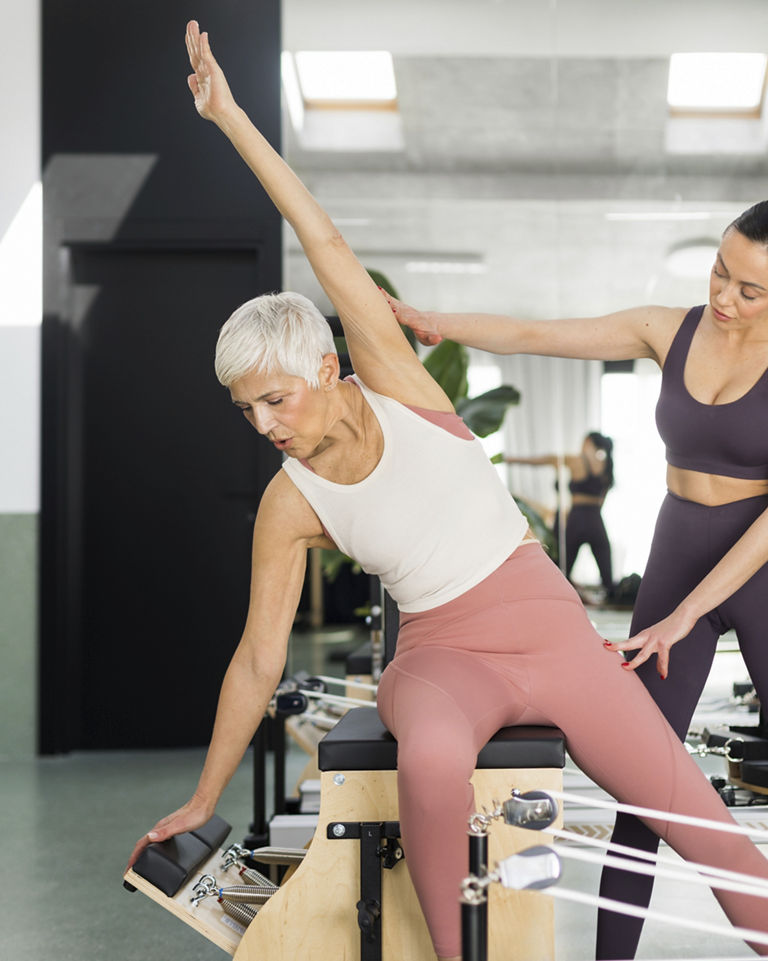 Beautiful senior woman having pilates class on performer machine with instructor