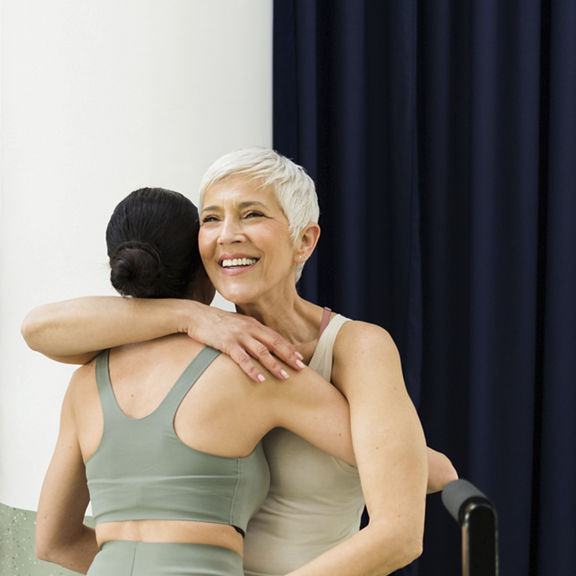 Two women greeting and hugging in pilates studio
