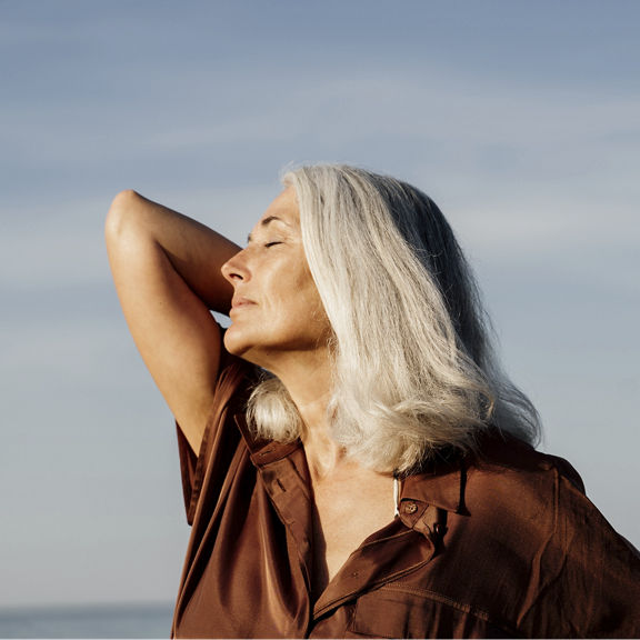 Active mature beautiful woman enjoying the beach in the morning wearing brown dress in front of the sea