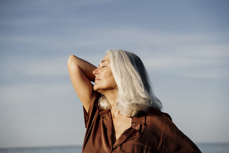 Active mature beautiful woman enjoying the beach in the morning wearing brown dress in front of the sea