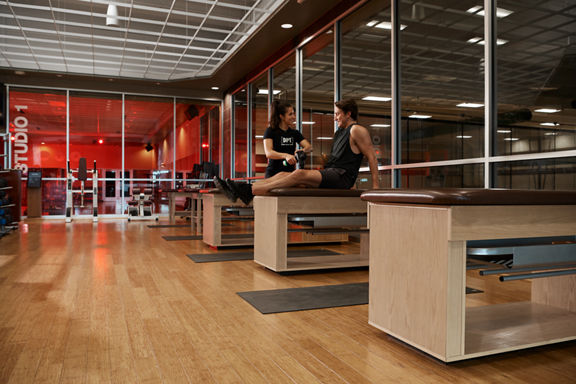 A female Dynamic Personal Trainer using a Hyperice device on a members thigh muscle