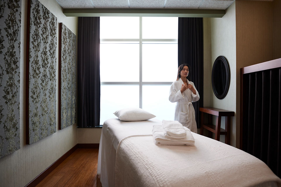 A female wearing a white robe standing next to a massage table