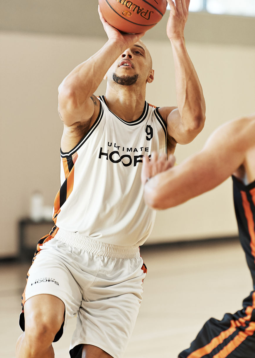 two males playing basketball - one making a shot, one blocking/defense