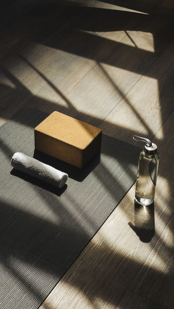 A waterbottle, yoga block, and towel sit by a yoga mat