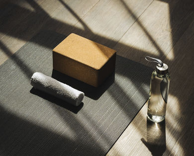 A waterbottle, yoga block, and towel sit by a yoga mat