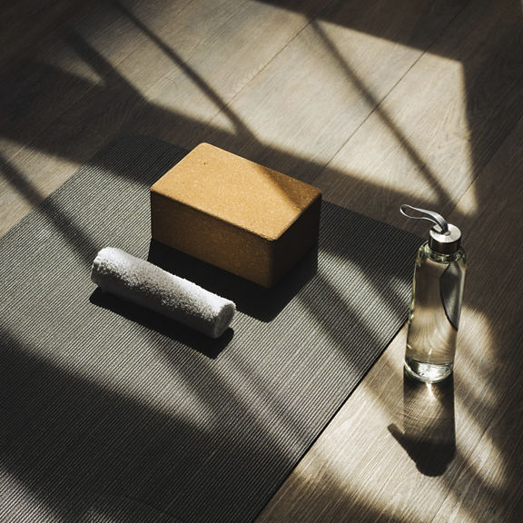 A waterbottle, yoga block, and towel sit by a yoga mat