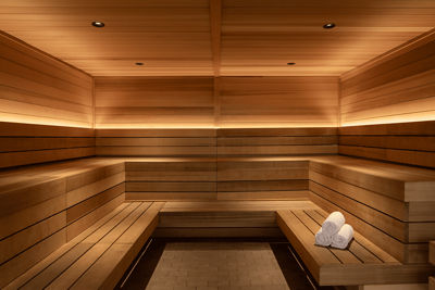 Modern wooden sauna with built-in benches on both sides, warm ambient lighting, and a stack of folded white towels on one of the benches.