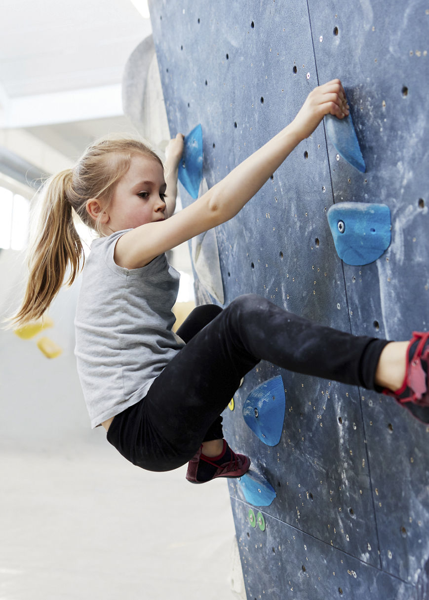 Girl climbing on a wall in bouldering gym