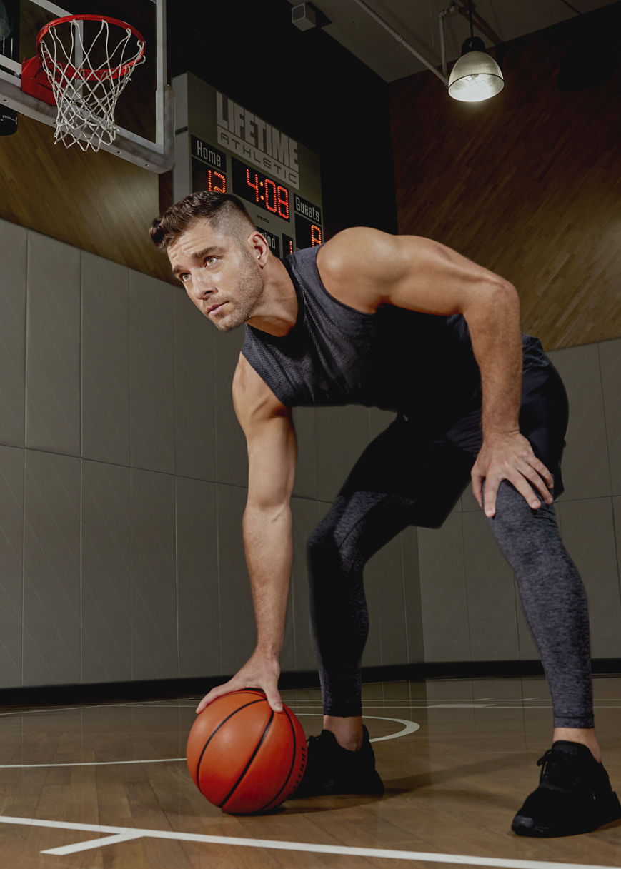 An adult man bent over holding a basketball on a wooden basketball court