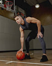 An adult man bent over holding a basketball on a wooden basketball court