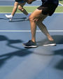 Women play pickleball on blue and green courty midday in Northern California, with stadium light fixture casting shadow on court.