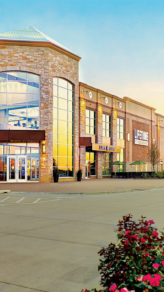 The exterior of a Life Time location on a sunny day with pink floral foliage