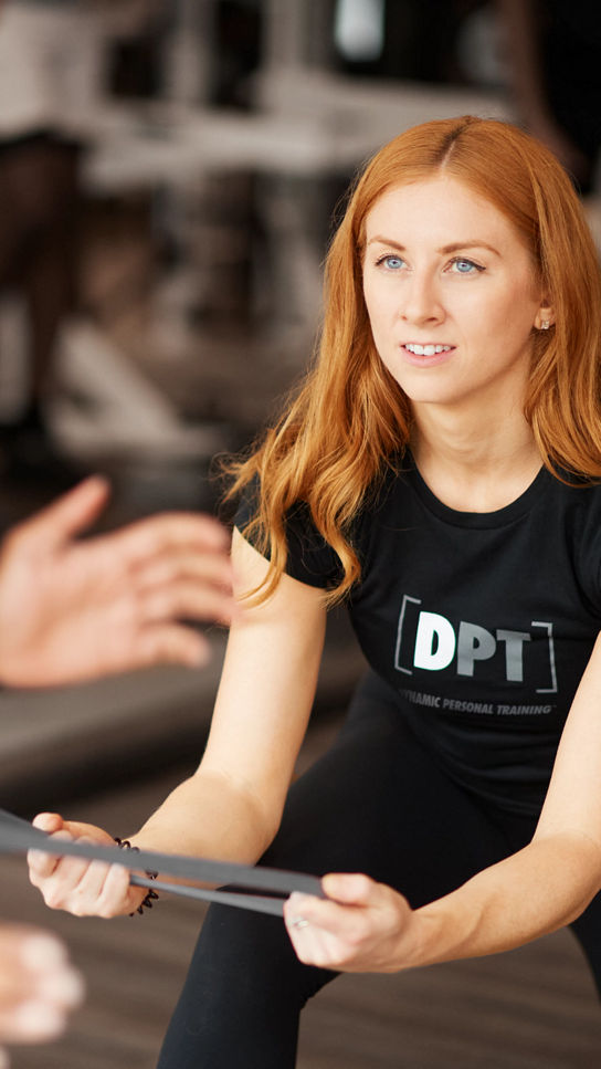 A female Life Time Dynamic Personal Trainer pulling on an athletic band wrapped around a participants waist