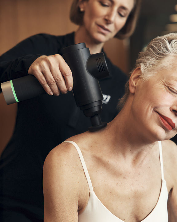 A Life Time Dynamic Personal Trainer massaging a client's neck with a massage gun