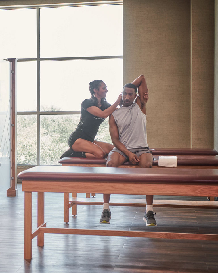 A Life Time Dynamic Personal Trainer stretching a man's arm while he sits on a stretch table