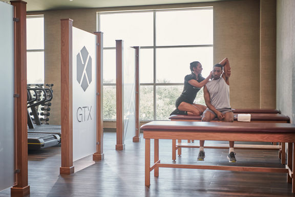 A Life Time Dynamic Personal Trainer stretching a man's arm while he sits on a stretch table