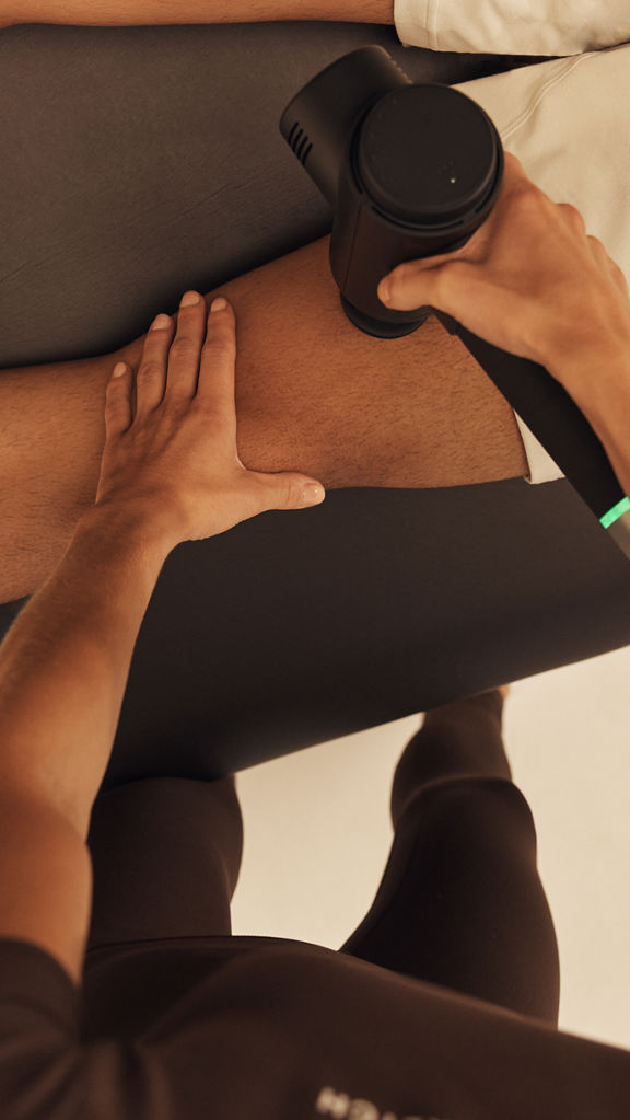 A Dynamic Personal Trainer using a massage gun on her client's leg