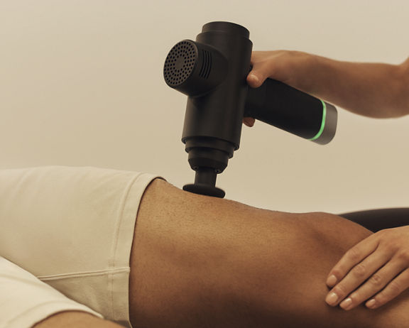 A Dynamic Personal Trainer using a massage gun on her client's leg