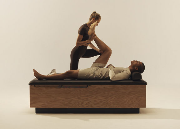 Trainer stretching a client's leg towards his chest while he lays on his back on a stretch table