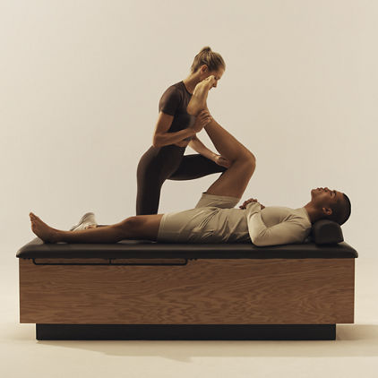 Trainer stretching a client's leg towards his chest while he lays on his back on a stretch table