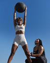 A Life Time Dynamic Personal Trainer providing support while a participant holds a medicine ball up over her head