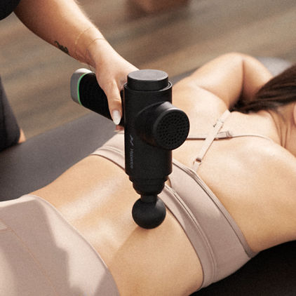 A Life Time Dynamic Stretch personal trainer using a hyperice massager on a woman's back while she lies on a table