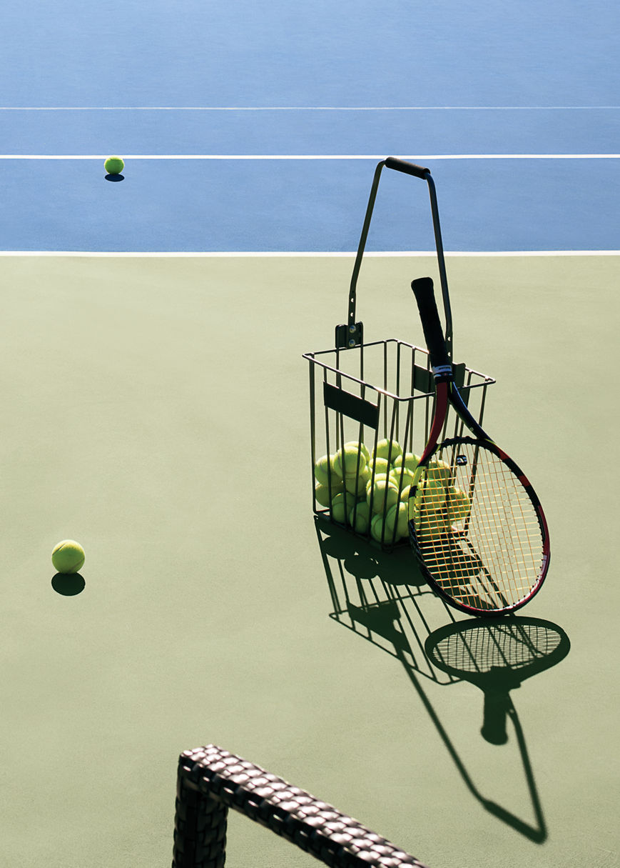 A basket of tennis balls and racquet on a tennis court