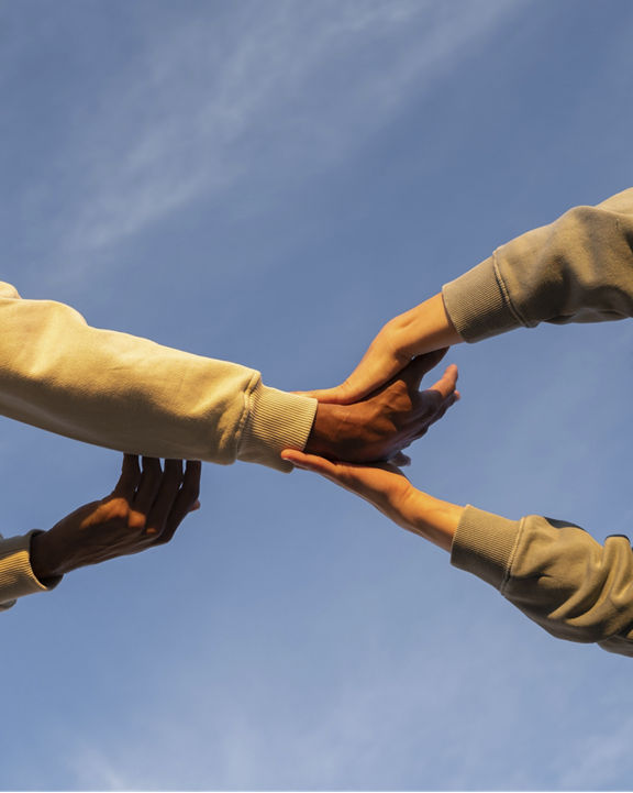 Low angle image of friends dancing and moving and holding hands against bright blue sky