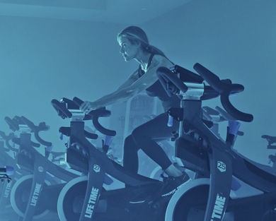 A female sitting on a stationary bike in a blue-lit cycle studio