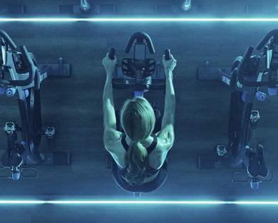 Overhead view of a female sitting on a stationary bike in a blue-lit cycle studio