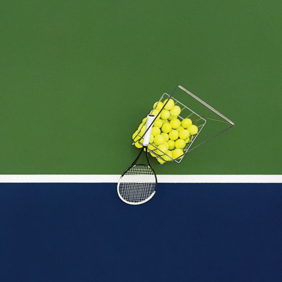 A basket of tennis balls and racquet on a tennis court