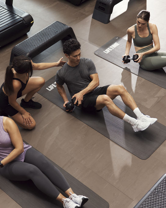GTX boutique group training class featuring three people doing weighted Russian twists