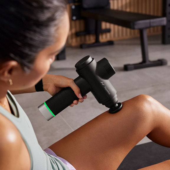 woman using a massage gun on her thigh