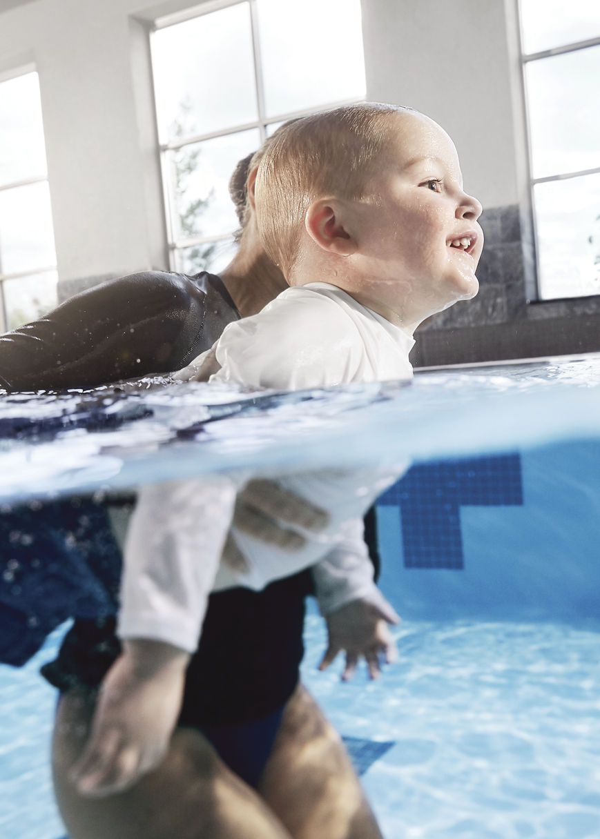 A swim instructor teaching a small child to swim in an indoor lap pool