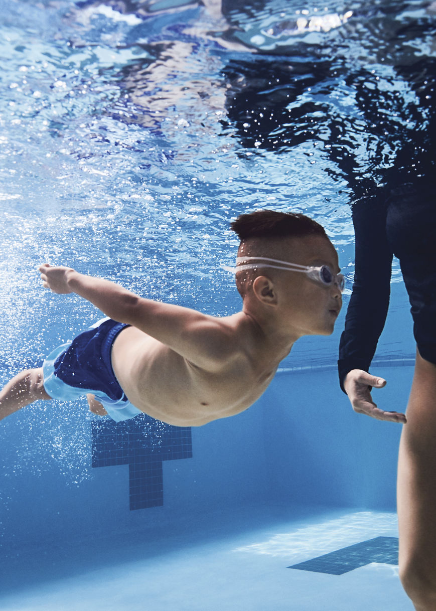 Underwater view of a swim instructor teaching a small child how to swim in an indoor pool