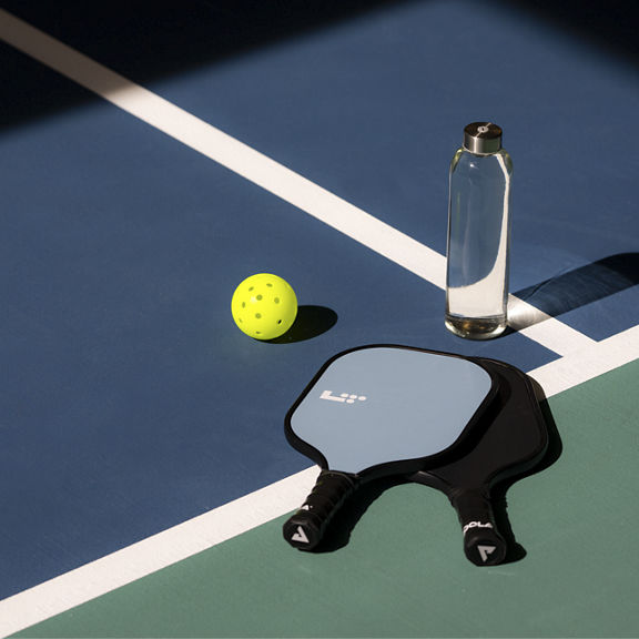 a pickleball, paddle and water bottle sitting on a pickleball court