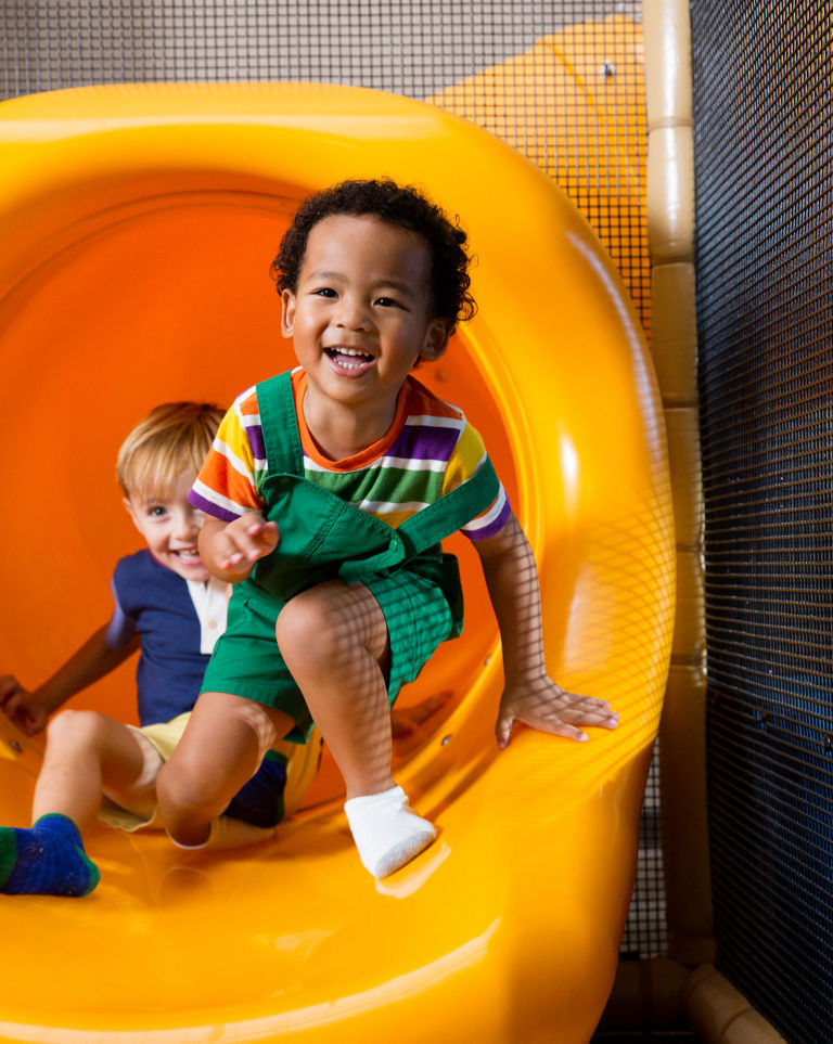 Two male children sliding out of an indoor playground slide