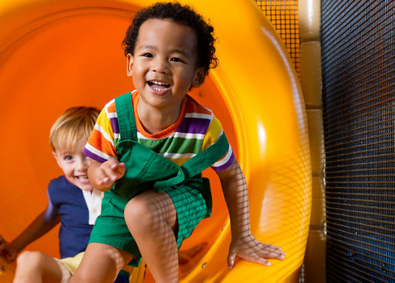 Two male children sliding out of an indoor playground slide