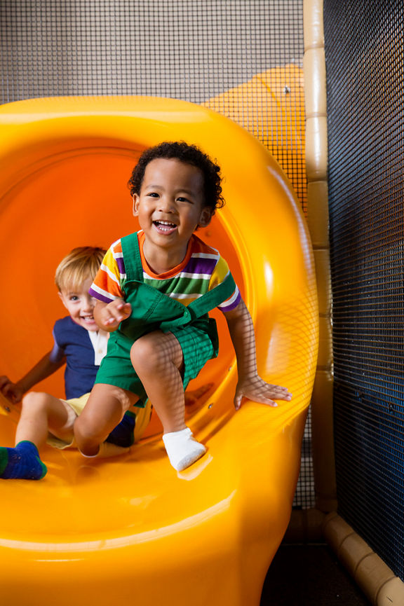 Two male children sliding out of an indoor playground slide