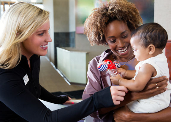 A woman holding and looking at a baby while a female Life Time team member stands next to them