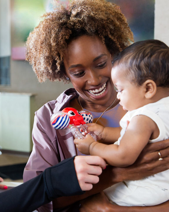 A woman holding and looking at a baby while a female Life Time team member stands next to them