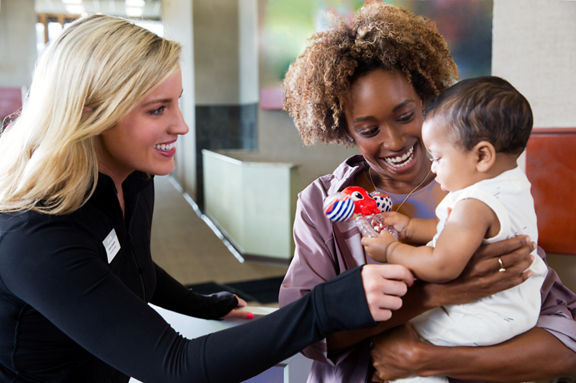 A woman holding and looking at a baby while a female Life Time team member stands next to them