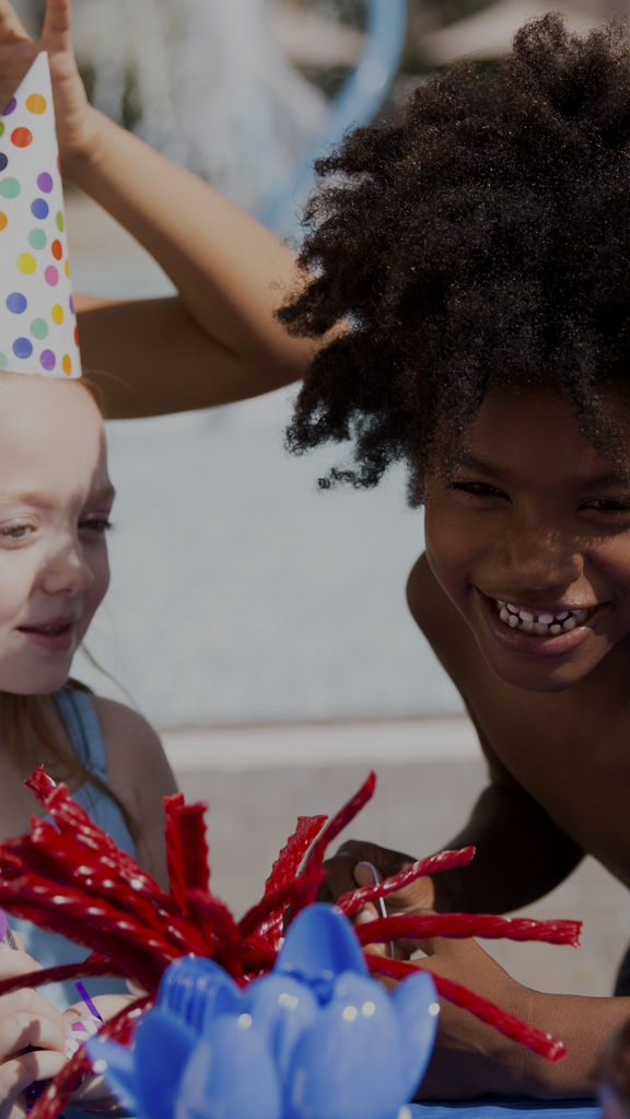 Four kids standing around a table with birthday cake and treats in an outdoor setting