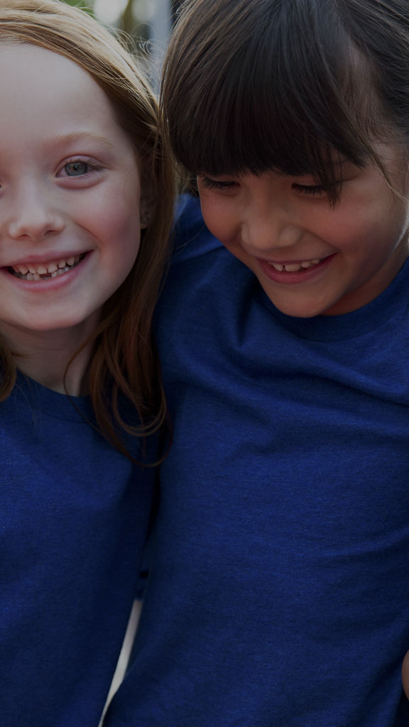 Close view of three female children wearing blue T-shirts huddled together with their arms around each other