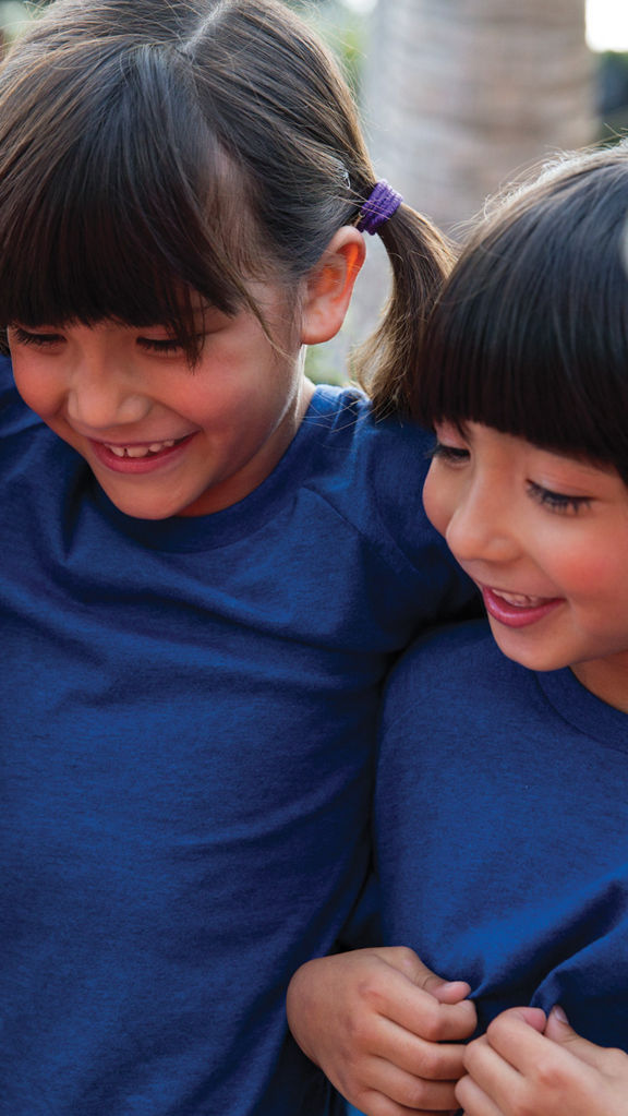 Close view of three female children wearing blue T-shirts huddled together with their arms around each other